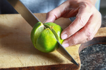 Chef cutting lime on wooden board, preparing preserved lemons