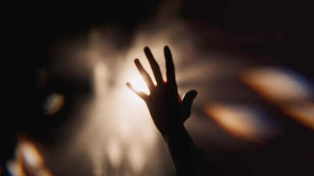 A hand is reaching in the light against a window for a faith or hope concept or spiritual belief idea. Photo animated with AI.