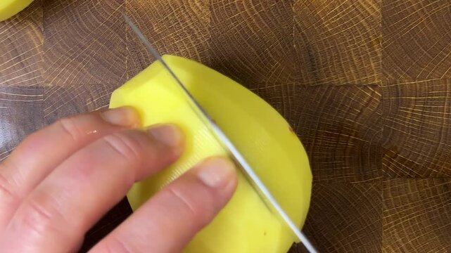 Chef chops potatoes with a knife on wooden cutting board.