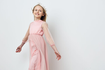A joyful young girl in a pink dress twirling with happiness against a simple white background,...