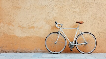 Naklejka premium Vintage white bicycle resting against textured beige wall in serene outdoor urban setting