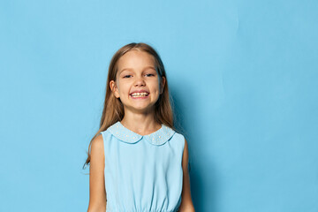 Little girl in a blue dress standing against a blue background with copy space for text or design...