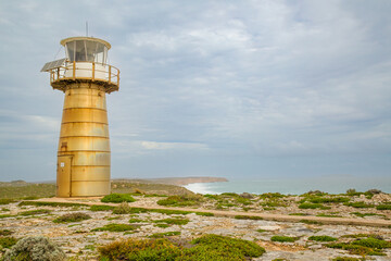 West Cape lighthouse, a stainless steel lighthouse, stands against a cloudy sky and on the sparsely vegetated and stony cliff tops above Spencer Gulf on the Yorke Peninsula in South Australia.