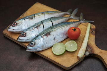 Some Fresh Mackerel Fish with slice of lemon, red tomato and lemon grass On Wooden Chopping Board,...