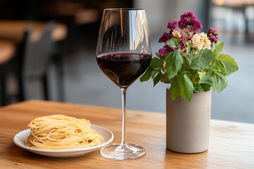 Naklejka premium A glass of red wine is on a table next to a plate of pasta