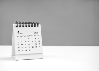 April 2025 page of desk calendar for organizer to plan and reminder, standing on white table on grey background with copy space. Small table calendar, front view, with the fourth month.