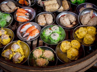 Various traditional food Chinese dim sum in mini bowls in large bamboo basket steamer, preparing in local restaurant, top view. Chinese dim sum takeaway finger food. Tasty Asian breakfast background.