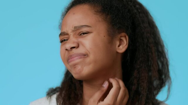 A pretty African American adolescent girl shows a thoughtful expression while scratching her neck. The vibrant blue background complements her features, highlighting her youth and individuality.