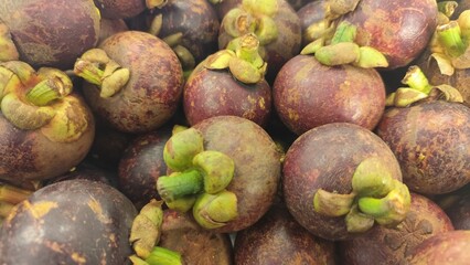 Close-up of a bunch of fresh mangosteens, showing their bright purple skin and green caps. Close-Up of fresh mangosteen background texture material.is a display in supermarket