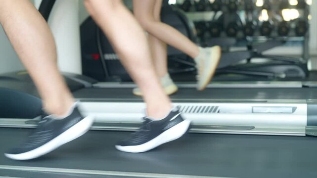 Healthy Asian man and woman sport training workout cardio exercise running on treadmills at fitness gym. Sportsperson checks heart rate and calories burned on smart watch. Health Technology concept.