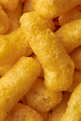 close-up macro view of crispy and spicy masala mix chips or yellow airy rice puffs in full frame background, deep fried bright golden snacks