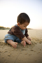 arafed baby boy sitting on the beach playing with sand
