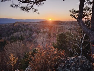 A tranquil sunset casts a warm glow over a sprawling forest, framed by mountains in the distance....