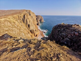 Breathtaking view of towering coastal cliffs meeting the expansive blue ocean under a clear sky. the rugged terrain and contrasting colors create a stunning natural landscape, capturing the tranquil