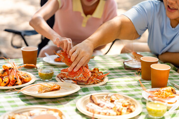 Happy man and woman travel at the sea on summer beach holiday vacation. Group of Asian people friends enjoy and fun outdoor lifestyle having lunch eating seafood together on tropical island beach.