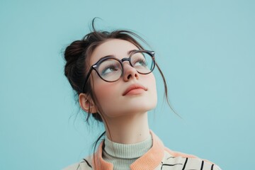 Young woman wearing glasses is looking upwards with thoughtful expression