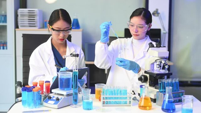 Two Asian female scientists in a high-tech lab analyzing biochemical samples, using micro pipettes,