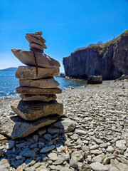 A peaceful coastal scene featuring a stack of balanced rocks on a pebble-covered beach. the calm sea and clear blue sky offer a tranquil backdrop, enhancing the natural beauty of the rocky shoreline