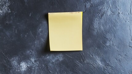 Slightly worn yellow sticky note stuck to a dark gray background creating a bold contrast for attention grabbing designs