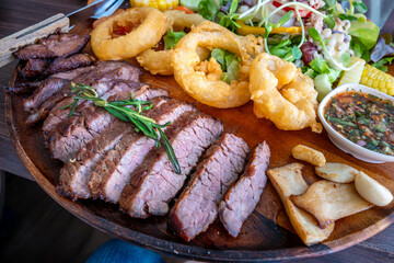A gourmet dining experience with a beautifully presented grilled beef platter, accompanied by crispy onion rings, a fresh garden salad, and thai style sauce.