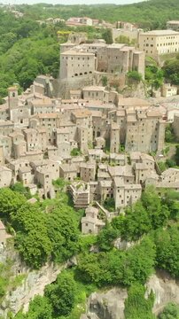 Aerial summer afternoon view of Sorano. Rooftops of an ancient medieval hill town hanging from a tuff stone over the Lente River. Etruscan heritage. Province Grosseto, Tuscany, Italy. Vertical footage