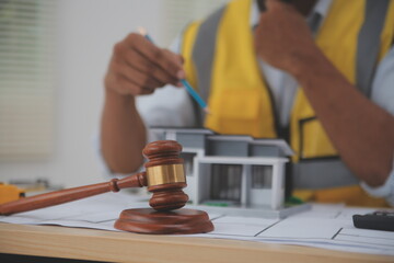 Judge gavel on building blueprint plans with a yellow safety helmet in the background. law that deals with matters relating to building construction, engineering. Construction law concept.