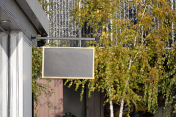 Blank sign hanging from a building in a sunny outdoor setting