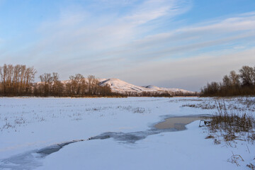 Winter landscape. Yenisei River on the border of the Republic of Khakassia and Krasnoyarsk Krai. Siberia, Russia. In the foreground, an ice-covered river. In the distance, snow-capped mountains.