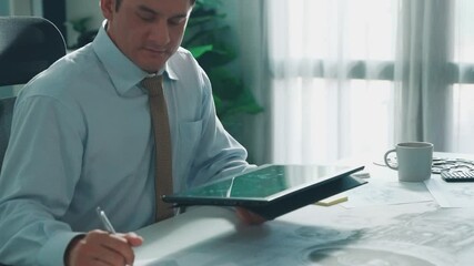 Professional engineer looking at phone while working on tablet with green screen at meeting table with turbine engine or jet engine sketch design and various metal gear scatter around. Alimentation.