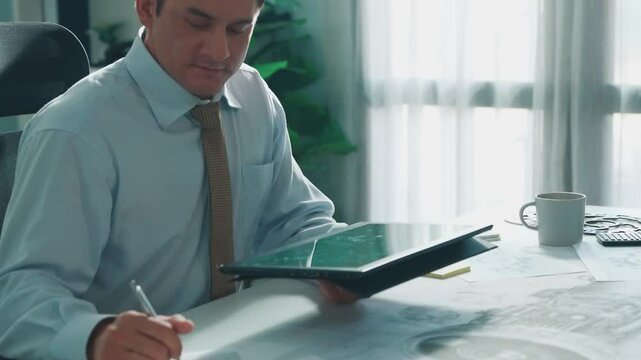 Professional engineer looking at phone while working on tablet with green screen at meeting table with turbine engine or jet engine sketch design and various metal gear scatter around. Alimentation.