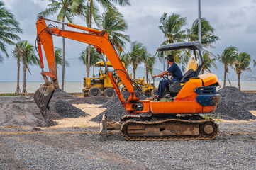 excavator at a gravel construction site on a beach by the sea performs excavation work on...