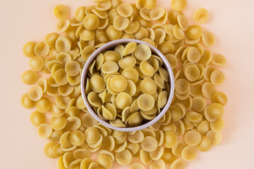 Top view of a porcelain bowl of raw italian durum wheat orecchiette pasta against a light ochre...