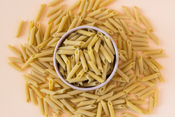 Top view of a bowl of raw italian durum wheat penne lisce pasta against a light ochre background . Raw dry penne lisce pasta in a bowl .