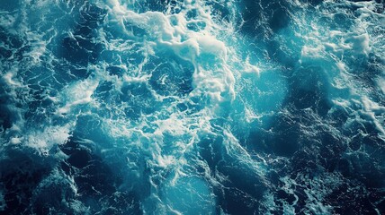 A close-up of ocean water with swirling currents and foamy crests, creating a dynamic and textured surface. The water is deep blue, with patches of lighter turquoise 