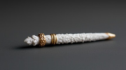 Obraz premium An ornate white carved stylus with detailed floral reliefs and gold bands rests on a dark grey surface.