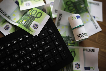 Computer keyboard and a scattering of 100 euro bills on the table. The work of a programmer and blogger on the Internet.