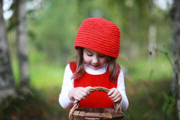 A little girl in a red hat and dresses is walking in the park. Cosplay for the fairytale hero "Little Red Riding Hood"