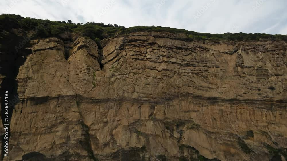 Poster zoom out video pulls back from a rocky cliff face with a complex, irregular surface under even, natu