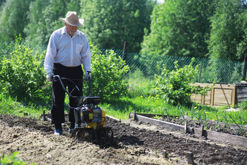 The farmer is digging a garden. A man with a harvester plows the garden. The gray-haired...