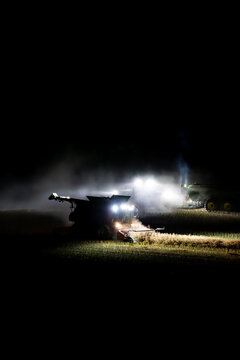 Harvester harvesting canola crop at night with chaser bin