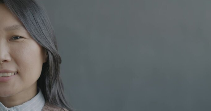 Close-up slow motion portrait of cheerful Asian lady half face looking at camera smiling on black color background. People and positive emotion concept.