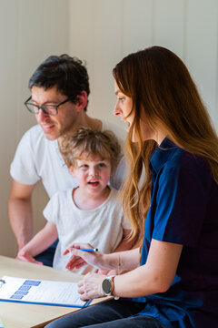 Parent with child talking with speech pathologist clinician holding paperwork during assessment