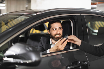 Caucasian male adult in business attire receives car keys while sitting in rented car. Represents convenience, transportation, and business travel.