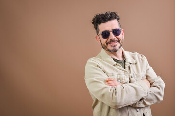 Obraz premium Smiling man with sunglasses and crossed arms on brown background