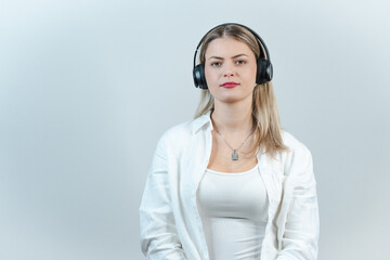 A joyful blonde woman in light-colored clothing listens to her favorite tunes with headphones,...