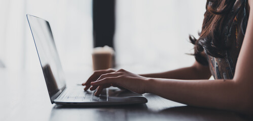 Young woman freelancer is typing on laptop keyboard, working remotely in cozy cafe with cup of...