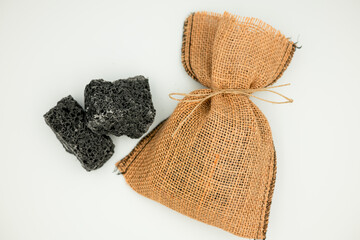 Natural burlap bag with black charcoal chunks on white background