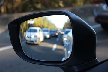 Exterior mirror of the car on a highway with slow moving defocused cars. Limited speed on highway...