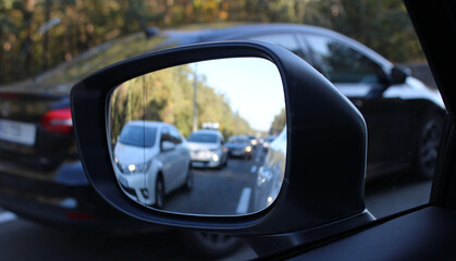 Forest road with blurred stopped cars reflects in the car mirror. Traffic jam on a country highway heading into the city on sunday evening before the start of the work week   
