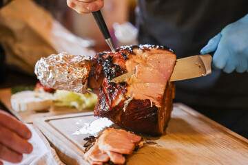 Person carving glazed Christmas ham on wooden cutting board